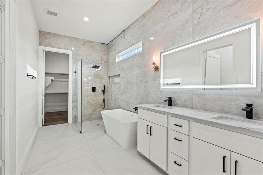 Bathroom with walk in shower, double vanity, a freestanding tub, a spacious closet, and tile walls