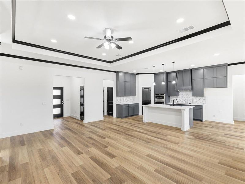 Unfurnished living room with crown molding, light wood-type flooring, ceiling fan, recessed lighting, and a tray ceiling Unfurnished living room with crown molding, light wood-type flooring, ceiling fan, recessed lighting, and a tray ceiling