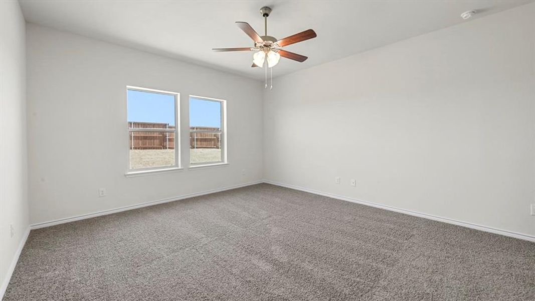 Spacious room featuring neutral carpet flooring, a ceiling fan with light fixture, and two windows