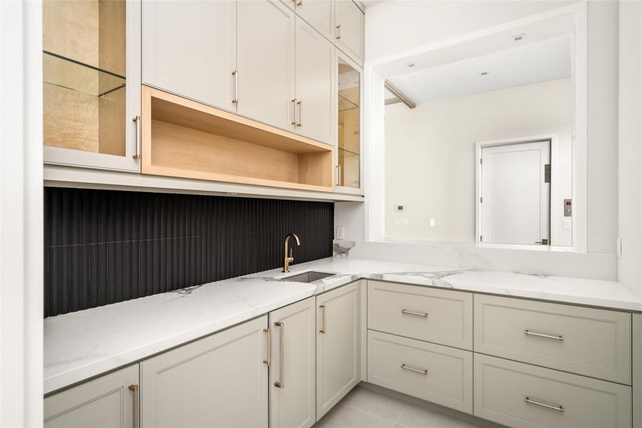 Well-appointed bar area featuring a navy linear tile backsplash, quartzite counters, and custom cabinetry with rift-cut white oak accents, complete with a sink, soft-close drawers, and built-in ice maker