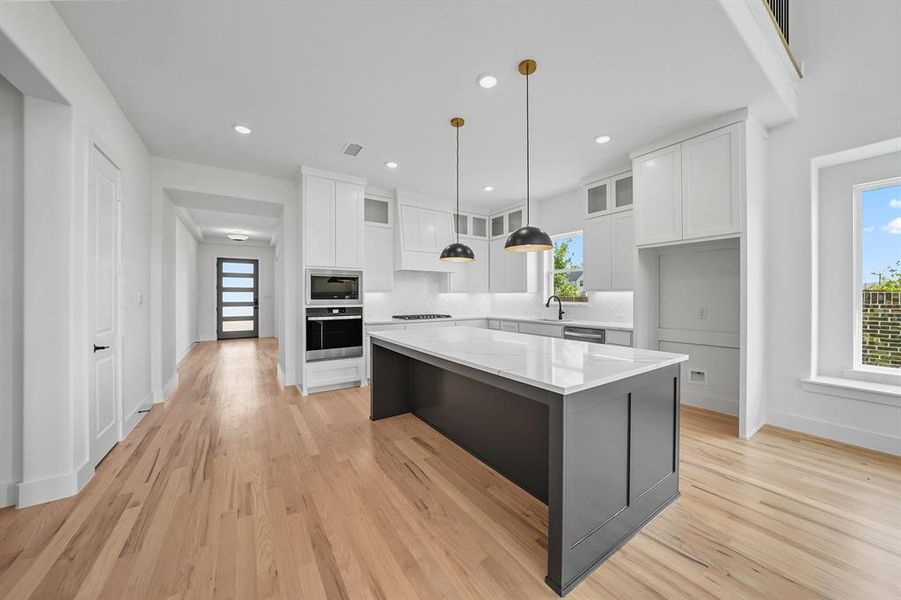 Kitchen with glass insert cabinets, white cabinetry, stainless steel appliances, pendant lighting, and light stone countertops