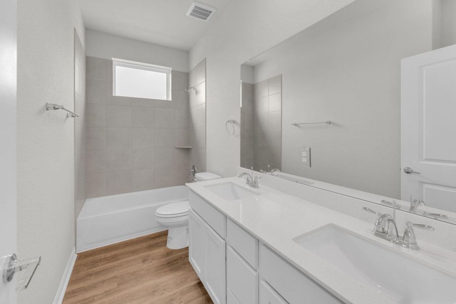 Bathroom featuring double vanity, bathtub / shower combination, and light wood-type flooring