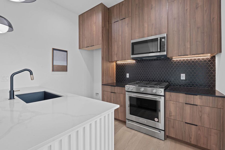 Kitchen featuring stainless steel appliances, modern cabinets, dark stone counters, tasteful backsplash, and light wood-type flooring