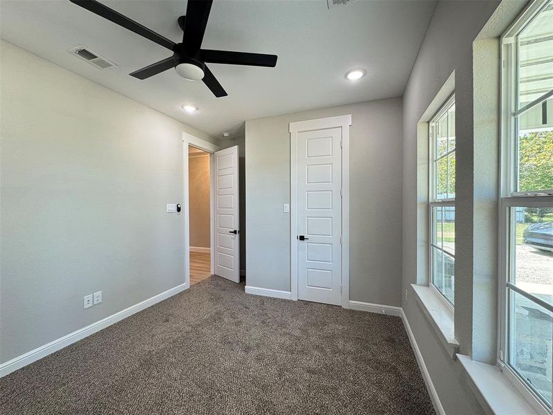 Carpeted interior room featuring a modern black ceiling fan, recessed lighting, and multiple windows with white trim
