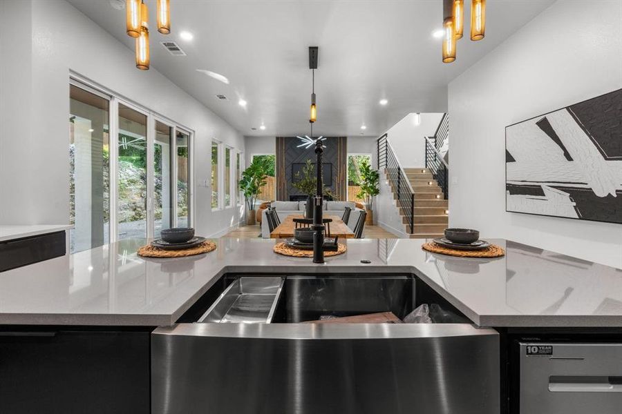 Kitchen with light stone countertops, stainless steel dishwasher, hanging light fixtures, open floor plan, and dark cabinets