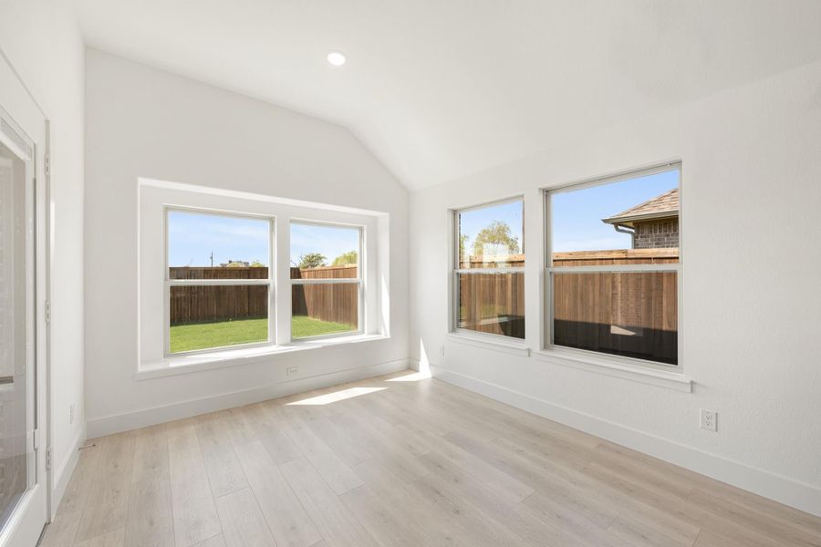 Empty room with vaulted ceiling, light hardwood floors, and four windows overlooking a fenced backyard