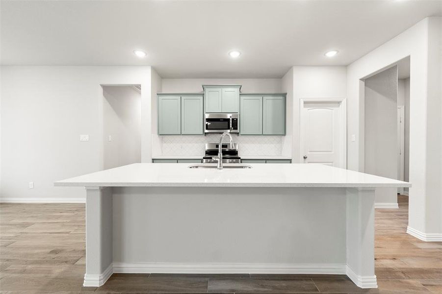 Kitchen with an island with sink, light stone counters, decorative backsplash, stainless steel appliances, and light wood-style flooring Kitchen with an island with sink, light stone counters, decorative backsplash, stainless steel appliances, and light wood-style flooring