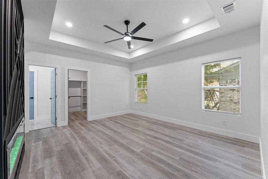 Unfurnished bedroom with ceiling fan, a tray ceiling, a spacious closet, and light hardwood / wood-style flooring