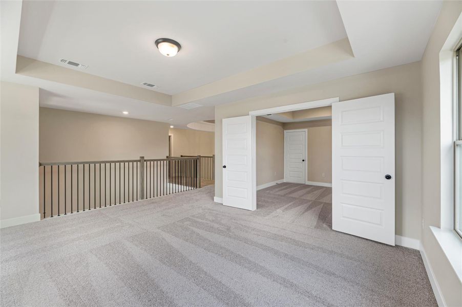 Carpeted spare room featuring a tray ceiling and baseboards