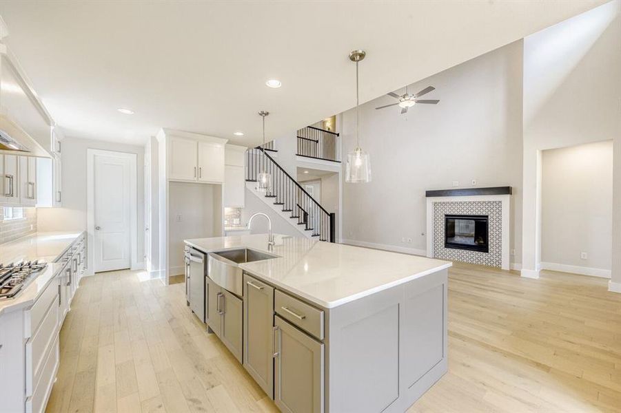 Kitchen featuring an island with sink, light wood finished floors, a tiled fireplace, hanging light fixtures, and open floor plan