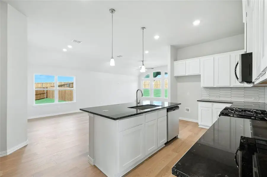 Kitchen with white cabinetry, ceiling fan, light wood-style floors, decorative light fixtures, and dark stone counters Kitchen with white cabinetry, ceiling fan, light wood-style floors, decorative light fixtures, and dark stone counters