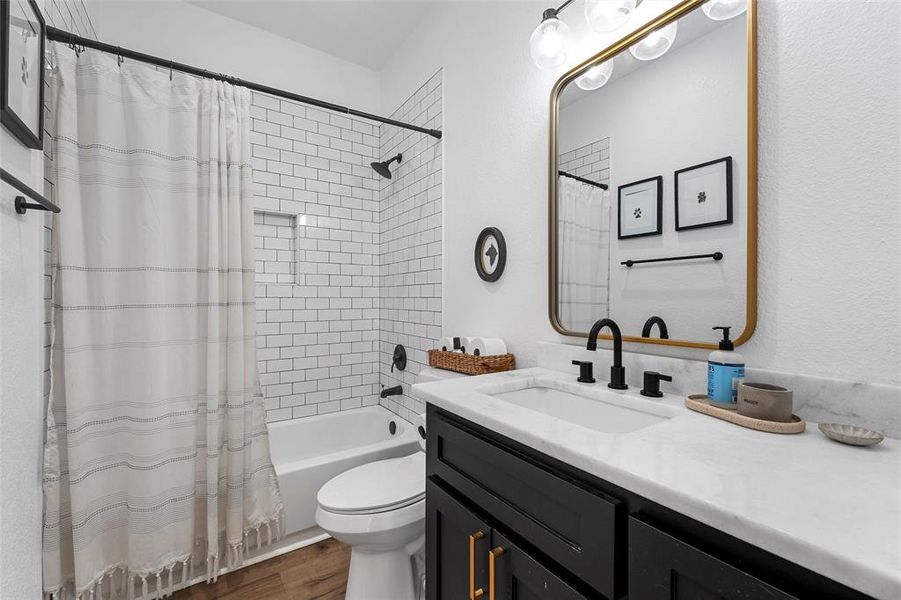 Bathroom featuring shower / bath combo with shower curtain, dark wood-style flooring, vanity, and a textured wall