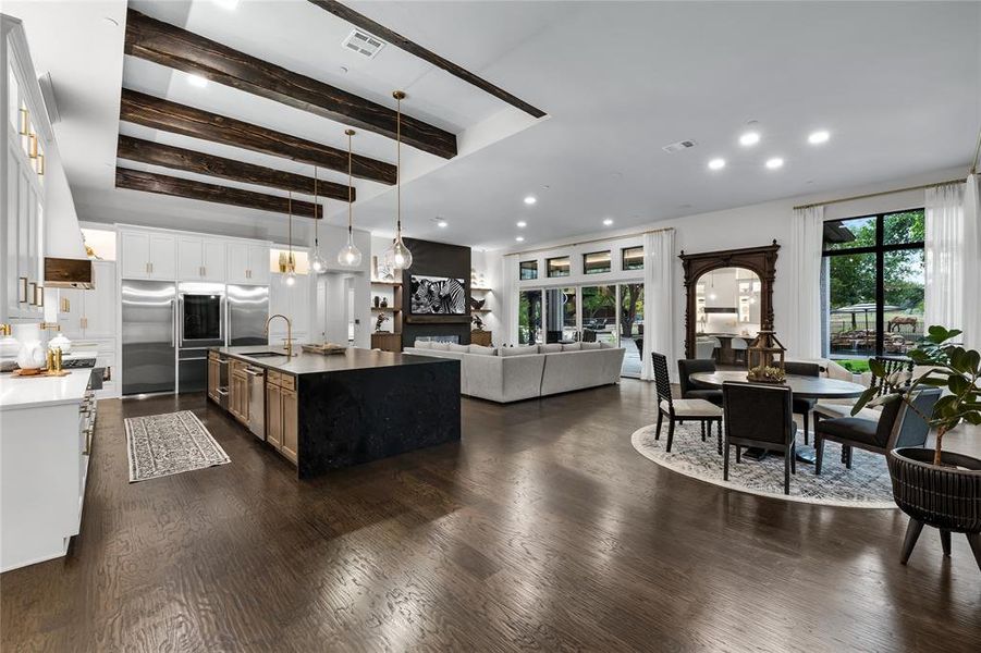 Kitchen with beam ceiling, white cabinetry, sink, pendant lighting, and a center island with sink