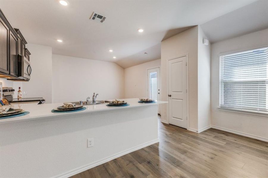Kitchen with black range with electric cooktop, a peninsula, stainless steel microwave, light wood-style flooring, and lofted ceiling Kitchen with black range with electric cooktop, a peninsula, stainless steel microwave, light wood-style flooring, and lofted ceiling