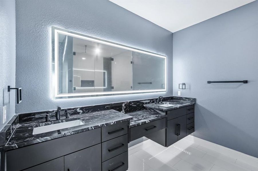 Bathroom featuring a stall shower, a textured wall, double vanity, and light tile patterned floors