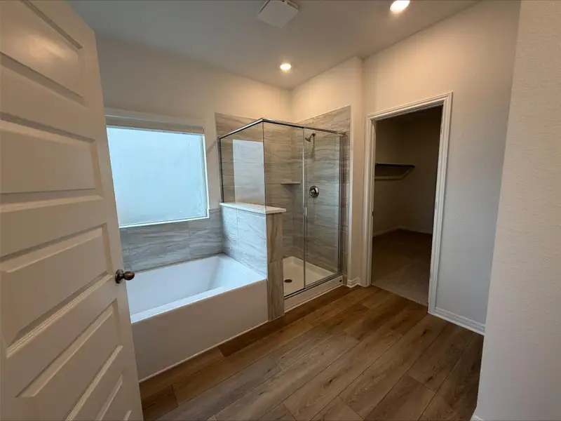 Full bathroom featuring light wood-style floors, a spacious closet, a garden tub, a stall shower, and recessed lighting Full bathroom featuring light wood-style floors, a spacious closet, a garden tub, a stall shower, and recessed lighting