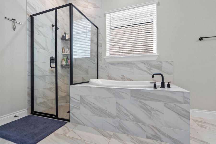 A glass-enclosed walk-in shower stands beside a tiled soaking tub under a window.