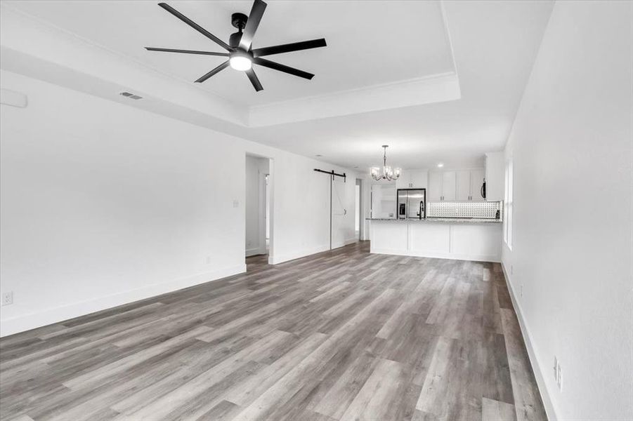 Unfurnished living room with light hardwood / wood-style floors, a tray ceiling, and ceiling fan with notable chandelier