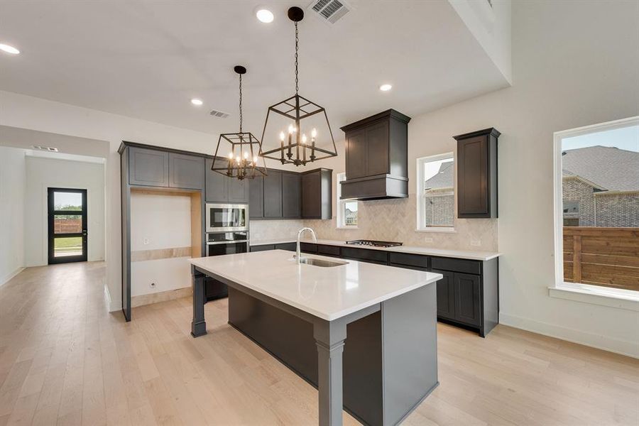 Kitchen featuring a center island with sink, decorative light fixtures, tasteful backsplash, light wood-style flooring, and a kitchen bar Kitchen featuring a center island with sink, decorative light fixtures, tasteful backsplash, light wood-style flooring, and a kitchen bar