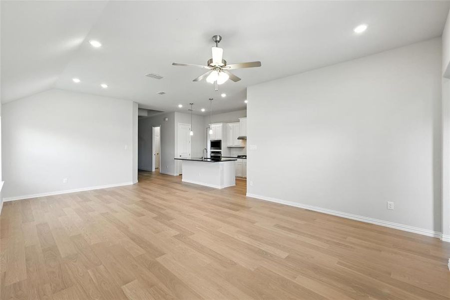 Unfurnished living room with a ceiling fan, recessed lighting, light wood finished floors, and lofted ceiling Unfurnished living room with a ceiling fan, recessed lighting, light wood finished floors, and lofted ceiling