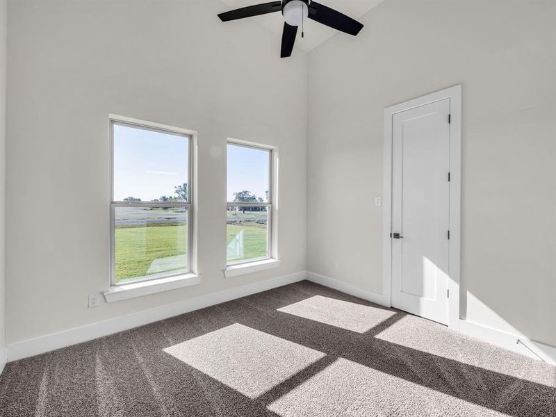 Unfurnished room featuring a towering ceiling, ceiling fan, and dark colored carpet