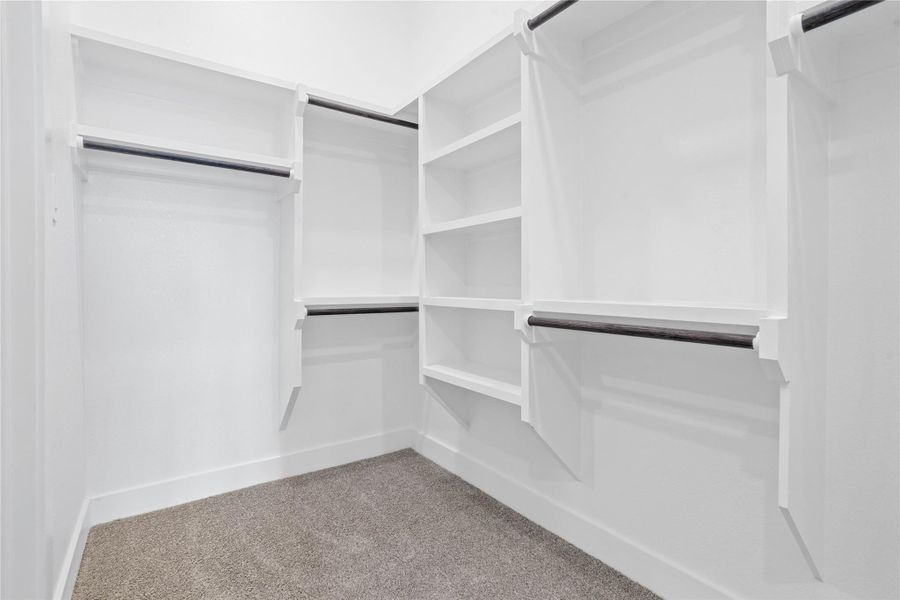 The spacious walk-in closet is equipped with clean white shelving and sturdy matte black hanging rods, offering extensive solutions for organizing an entire wardrobe. This closet also features direct access to the laundry room, a dream feature for modern living.