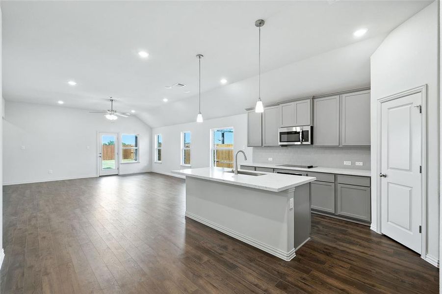 Kitchen featuring gray cabinets, lofted ceiling, hanging light fixtures, decorative backsplash, and a center island with sink Kitchen featuring gray cabinets, lofted ceiling, hanging light fixtures, decorative backsplash, and a center island with sink