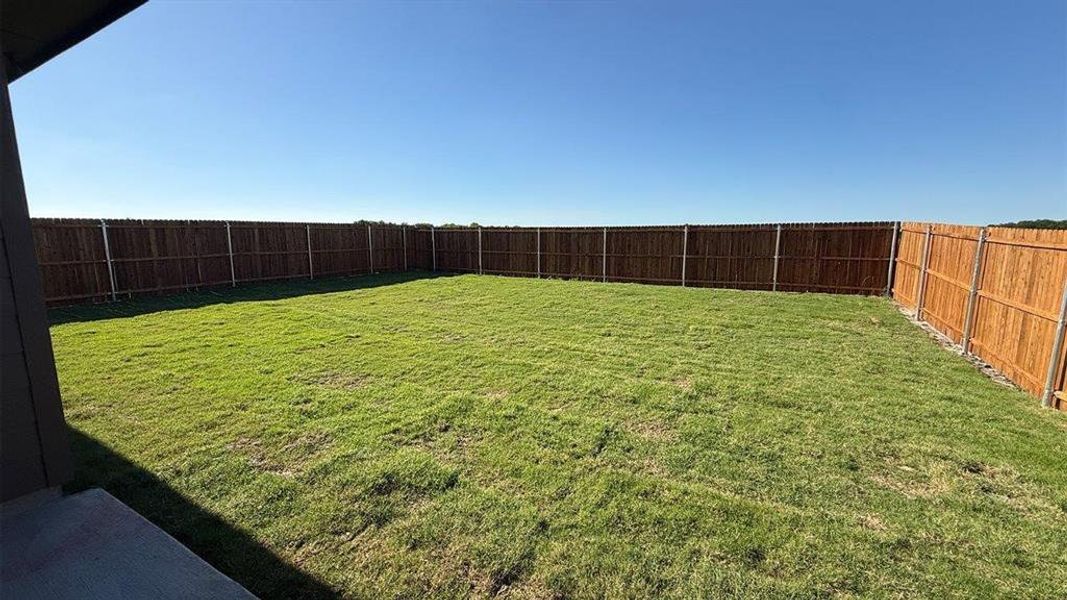 Fenced backyard featuring a large grass area and a concrete patio