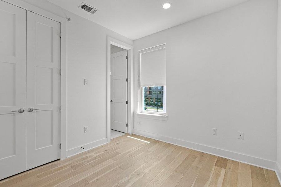 A quiet bedroom retreat features light wood flooring and ample natural illumination from a single window. A quiet bedroom retreat features light wood flooring and ample natural illumination from a single window.