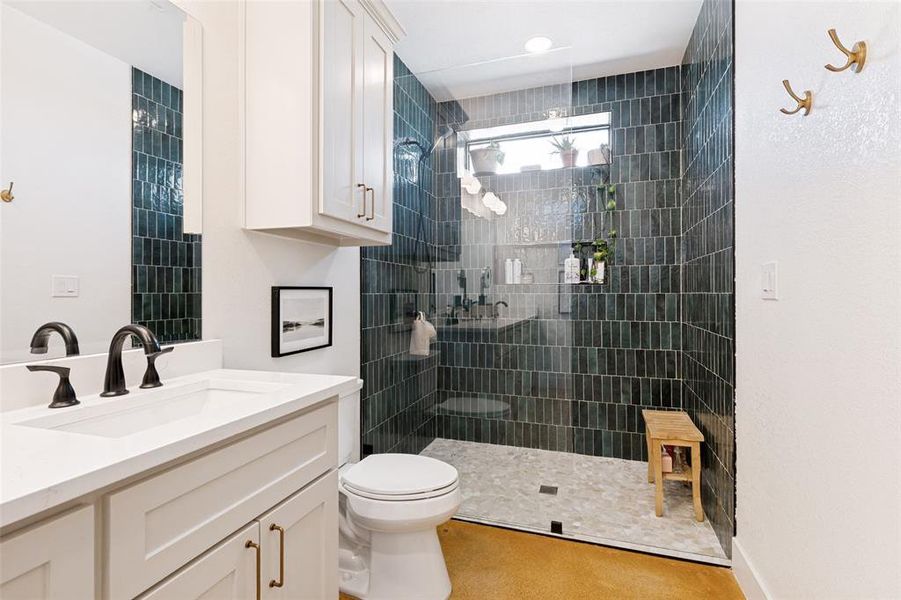 Bathroom featuring a walk-in shower with dark emerald subway tile, a white vanity with quartz countertop, dual matte black faucets, and a built-in wall cabinet Bathroom featuring a walk-in shower with dark emerald subway tile, a white vanity with quartz countertop, dual matte black faucets, and a built-in wall cabinet