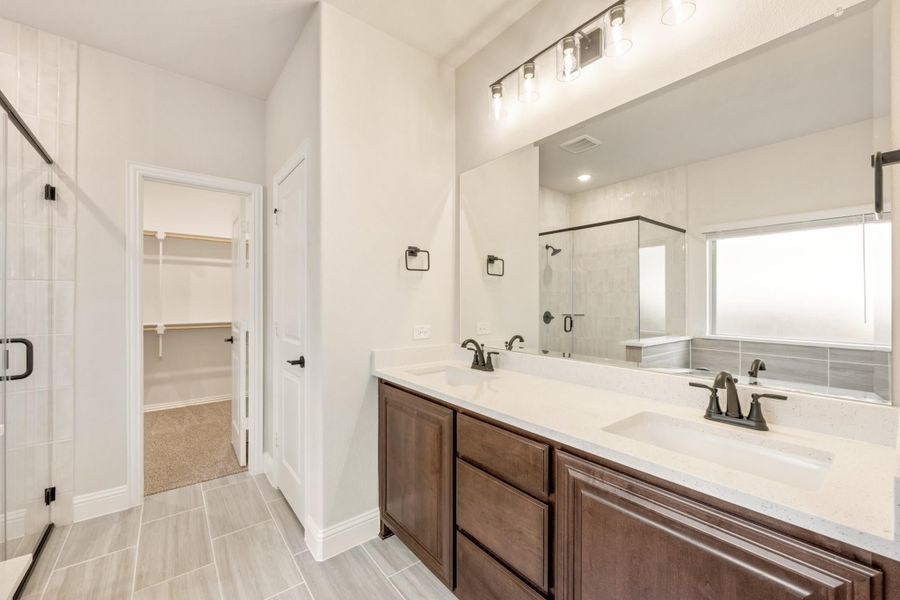 Bathroom with double vanity, dark wood cabinets, glass shower, and walk-in closet entrance