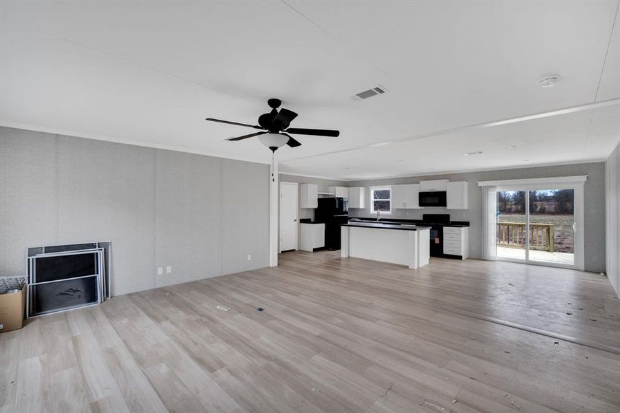 Unfurnished living room featuring light wood-style flooring, a ceiling fan, and ornamental molding