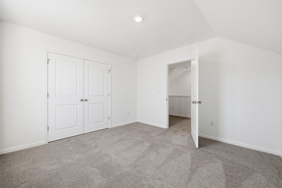 Unfurnished bedroom with light carpet, a closet, and vaulted ceiling Unfurnished bedroom with light carpet, a closet, and vaulted ceiling