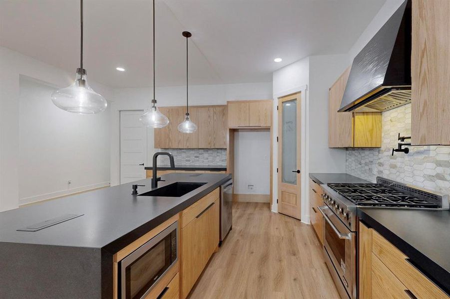 Contemporary kitchen featuring light wood-finish cabinetry, dark countertops, and wood-finish flooring Contemporary kitchen featuring light wood-finish cabinetry, dark countertops, and wood-finish flooring