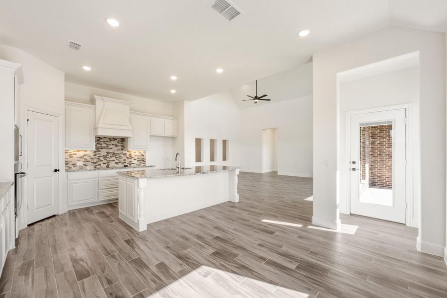 Open kitchen with white cabinets, granite island, tile backsplash, and wood-look floors opening to living area Open kitchen with white cabinets, granite island, tile backsplash, and wood-look floors opening to living area