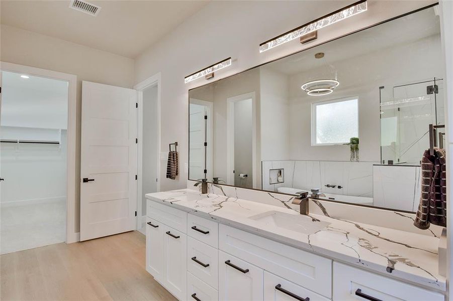 Bathroom with double vanity, a stall shower, a walk in closet, and light wood-type flooring Bathroom with double vanity, a stall shower, a walk in closet, and light wood-type flooring
