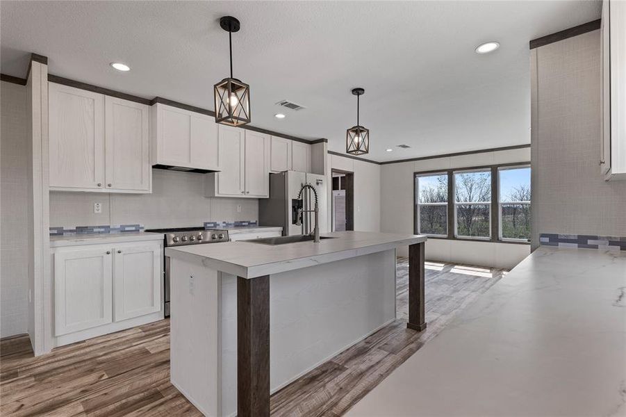 Kitchen with light countertops, stainless steel appliances, hanging light fixtures, white cabinets, and light wood-style flooring