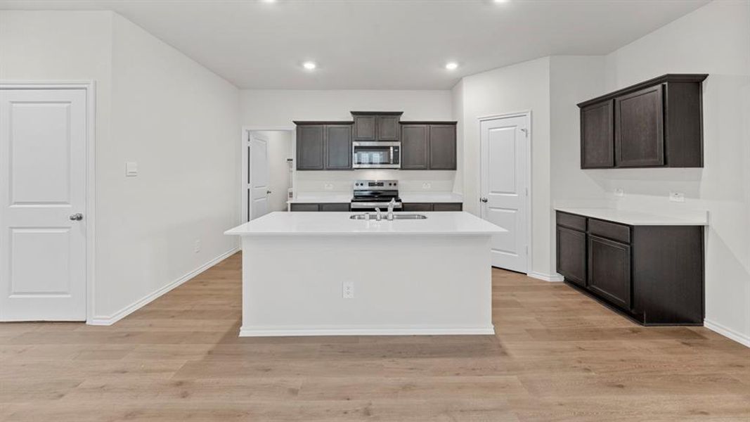 Kitchen featuring appliances with stainless steel finishes, an island with sink, light wood-style floors, recessed lighting, and light stone countertops