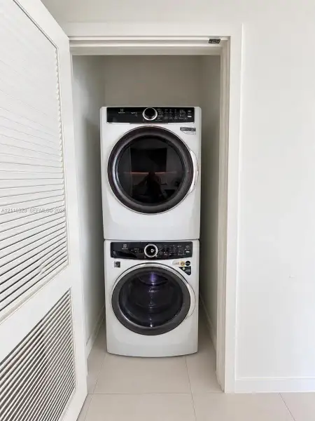 Stacked laundry center featuring a high-efficiency front-load washer and dryer set, housed within a closet with louvered bi-fold doors