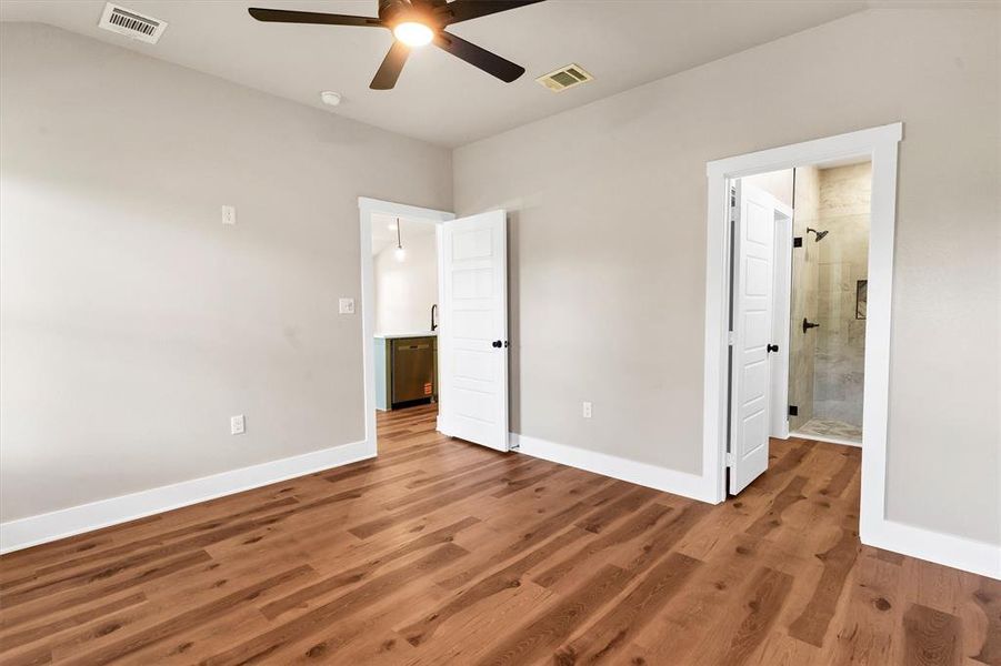 Unfurnished bedroom with wood finished floors, ceiling fan, connected bathroom, and vaulted ceiling Unfurnished bedroom with wood finished floors, ceiling fan, connected bathroom, and vaulted ceiling
