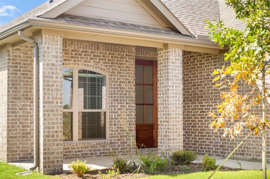 Doorway to property featuring brick siding and roof with shingles