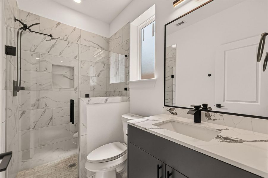 This modern bathroom features a sleek design with a glass-enclosed shower, marble-patterned tiles, and a stylish dark vanity with a contemporary sink and fixtures. A frosted window provides natural light while maintaining privacy. This modern bathroom features a sleek design with a glass-enclosed shower, marble-patterned tiles, and a stylish dark vanity with a contemporary sink and fixtures. A frosted window provides natural light while maintaining privacy.