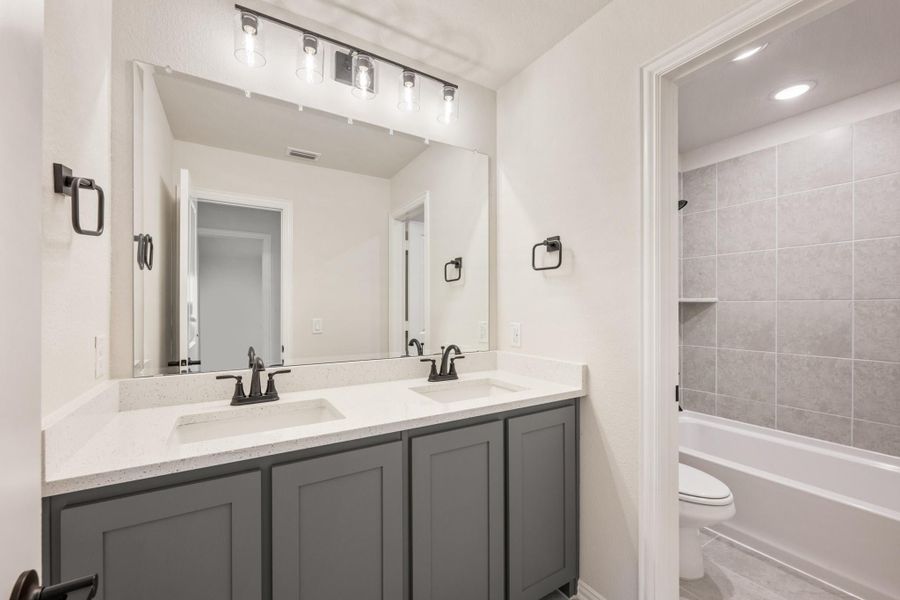 Bathroom with double sink vanity, gray cabinets, white countertop, and tiled tub-shower combo Bathroom with double sink vanity, gray cabinets, white countertop, and tiled tub-shower combo