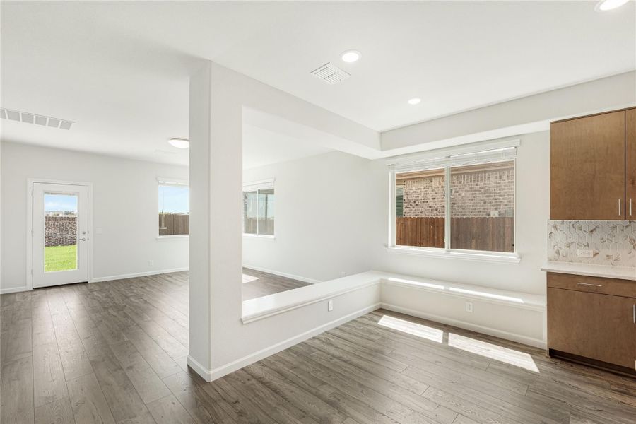 Open-plan dining and living area with hardwood floors, built-in bench seating, and wood cabinets nearby