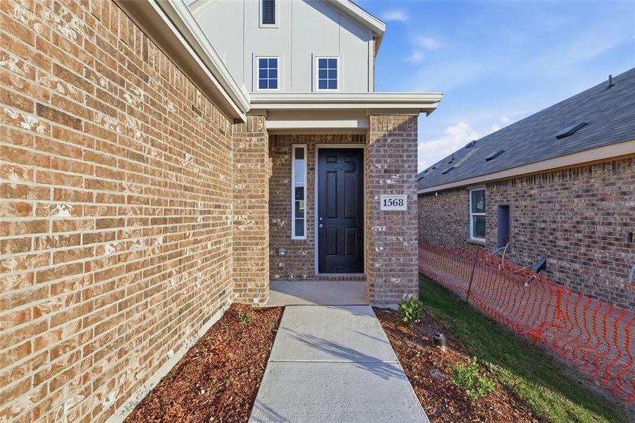 Brick facade home featuring a covered entryway, a dark paneled front door, white window trim, and a concrete walkway