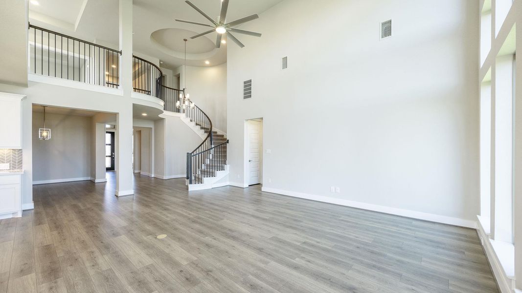 Unfurnished living room with stairs, light wood-style floors, a ceiling fan, and a towering ceiling Unfurnished living room with stairs, light wood-style floors, a ceiling fan, and a towering ceiling