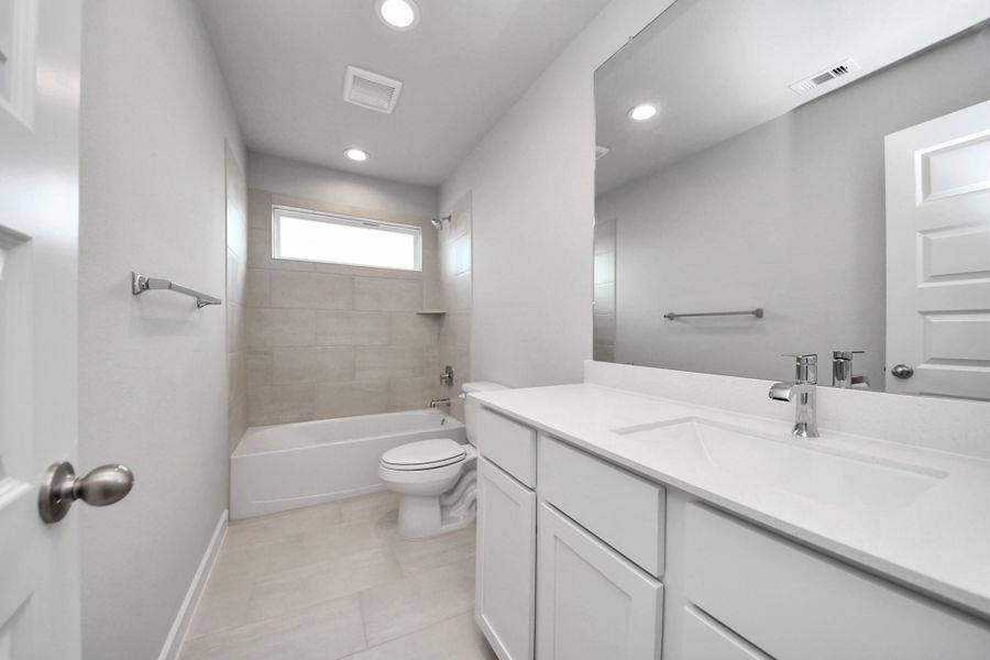 Secondary bath features tile flooring, bath/shower combo with tile surround, light stained wood cabinets, beautiful light countertop.
