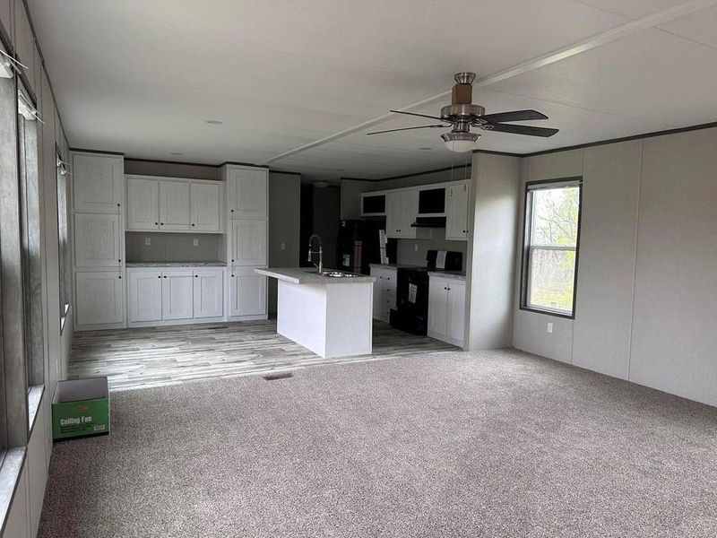 Kitchen with open floor plan, black appliances, an island with sink, white cabinets, and light countertops Kitchen with open floor plan, black appliances, an island with sink, white cabinets, and light countertops