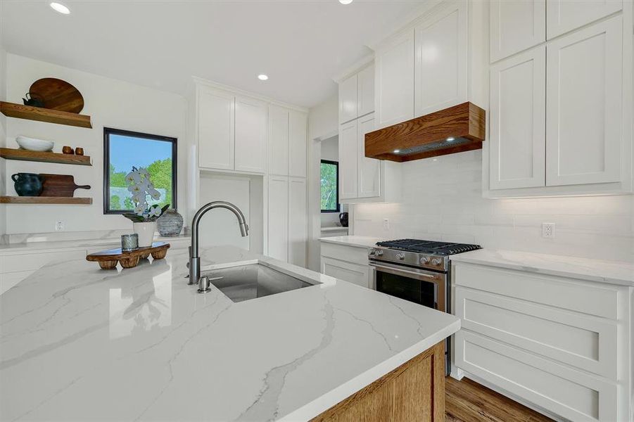 Kitchen with decorative backsplash, light stone counters, white cabinets, premium range hood, and sink