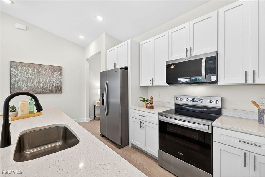 Kitchen featuring appliances with stainless steel finishes, white cabinetry, light wood-style floors, light stone counters, and recessed lighting